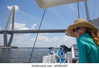 A young woman pilots a sailboat under the Ravenel Bridge in Charleston, South Carolina.