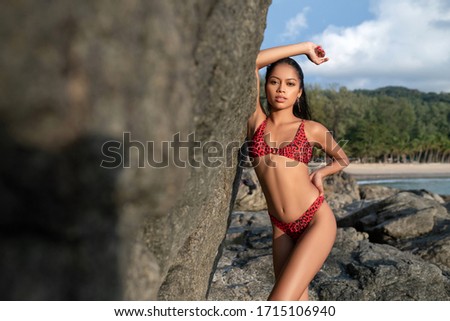 Young woman in pink bikini posing near rocks on the tropical beach. Trip to warm destination
