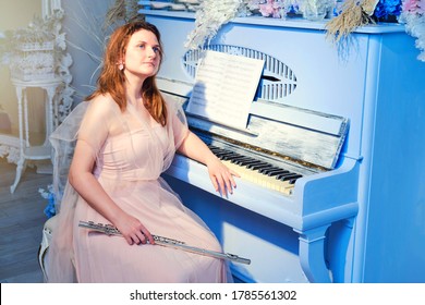 A young woman in a pink dress is sitting at an old piano. Musician with a flute near a retro piano