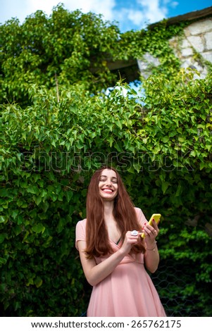 Young woman in pink dress using mobile phone on green ivy background