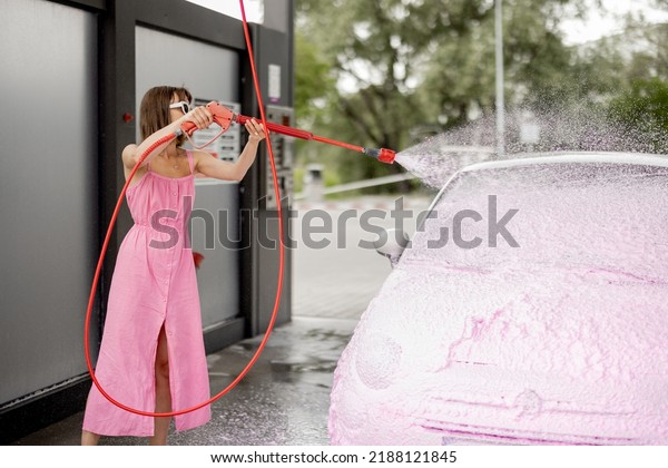 Young woman in pink dress washing her tiny car\
with nano foam at car wash during summer time. Easy and beautiful\
self-service at car wash\
concept