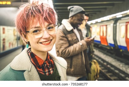 Young woman with pink hair and group of multiracial hipster friends waiting for train at tube subway station - Urban friendship concept with young people standing together in city underground area