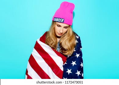 Young Woman In A Pink Hat On A Vibrant Blue Background Holding The American Flag On The Forth Of July. The Concept Of National Holidays And Independence Day Of Independence Of America July 4