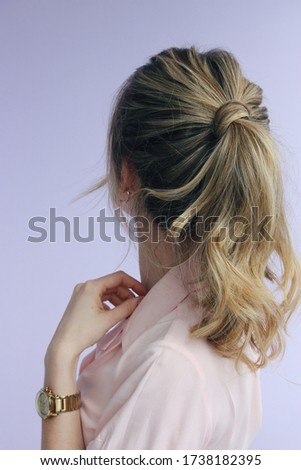 young woman in a pink lapel collar short sleeve shirt with a messy twisted balayage ponytail and golden accessories back view photo