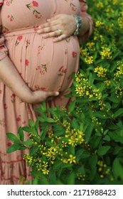 A young woman in  pink printed tight-fitting dress embraces her belly with a future baby with trepidation and tenderness.  yellow flowers .  selective focus" " follow focus" " shallow depth of field" 