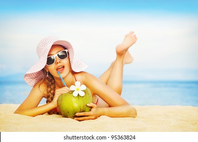 Young woman in pink swimsuit with coconut cocktail on the beach, bali