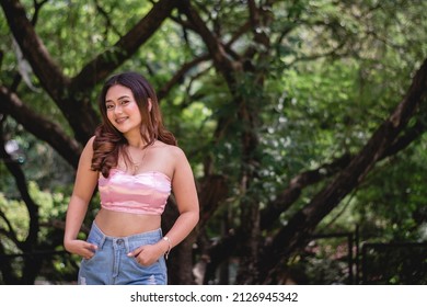 A young woman in a pink tube top and jeans smiles towards the camera. Perfectly showing her confidence and simplicity.