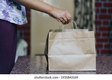 Young woman placing a brown paper food delivery package on a table. Recyclable, eco friendly, zero waste packaging