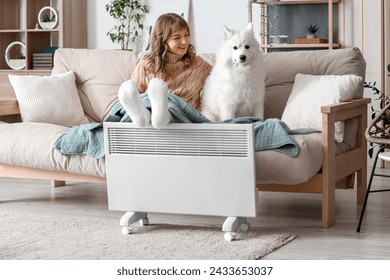 Young woman with plaid and her Samoyed dog warming legs on radiator at home - Powered by Shutterstock