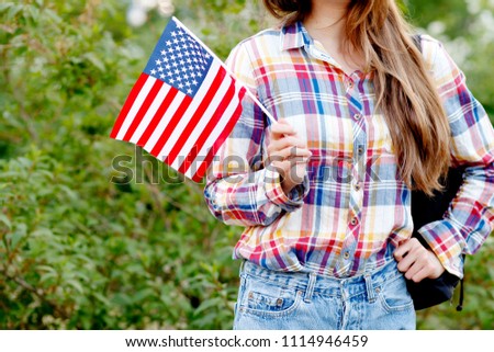 Young woman in plaid shirt and shorts holding out an American flag in the outdoors. Independence Day (United States) 