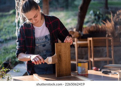 Young woman in a plaid shirt varnishing a wooden detail on a shelf on the terrace 
