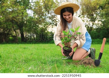 Young woman planting tree in garden, space for text