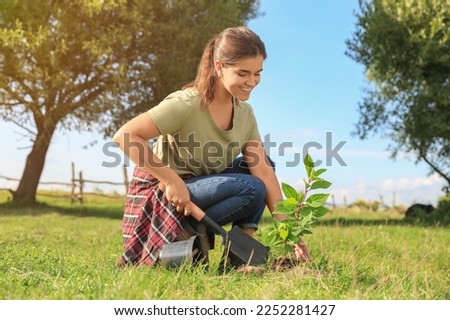 Young woman planting tree in garden on sunny day