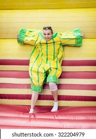 Young Woman In Plastic Dress In A Bouncy Castle Imitates A Fly On Velcro Wall. Inflatable Attraction.