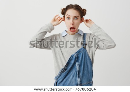 Young woman playfully posing on camera with open mouth grimacing having fun. Schoolgirl in casual clothes fooling around making ears protruding instead of studying. Attitude, position concept