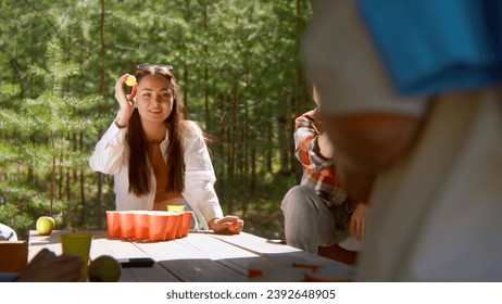 Young woman playing beer pong. Stock footage. Beautiful woman throws ball into glass of beer. Fun game for friends with alcohol and ping pong in nature in summer - Powered by Shutterstock