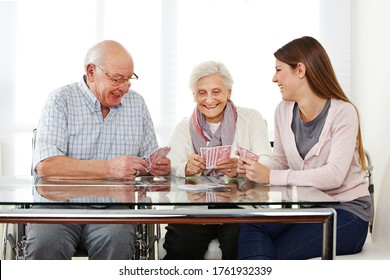 Young Woman Playing Cards With Two Happy Seniors In Nursing Home