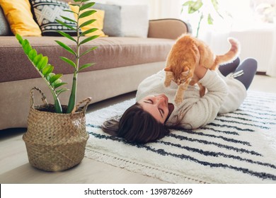Young woman playing with cat on carpet at home. Master lying on floor with her pet