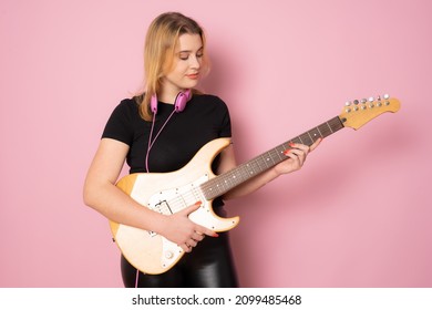 Young Woman Playing The Electric Guitar Standing Over Pink Background.