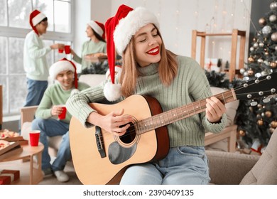 Young woman playing guitar at Christmas party with her friends - Powered by Shutterstock