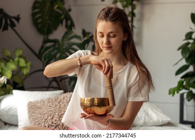 Young woman playing on a singing tibetian bowl.Relaxation and meditation.Sound therapy,alternative medicine.Buddhist healing practices.Clearing the space of negative energy.Selective focus,close up.