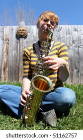 Young Woman Is Playing A Shiny Saxophone Sitting Outdoors With Green Grass And Blue Sky (focus On Saxaphone)