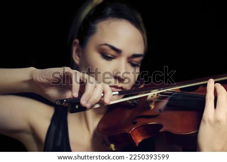 Young woman playing violin, hands in focus, black background
