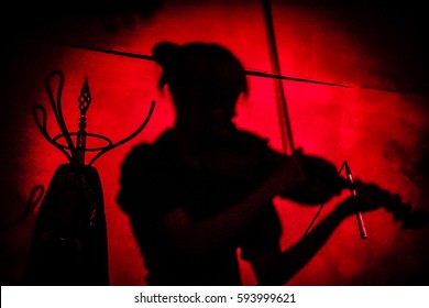 Young Woman Playing The Violin. Violinist Silhouette On Stage. Red Ligth