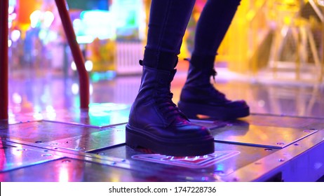 A Young Woman Plays Dancing In An Amusement Park. A Girl Plays With Her Legs In A Slot Machine. Legs Close Up. Park For Children With Slot Machines And Bright Light Bulbs.