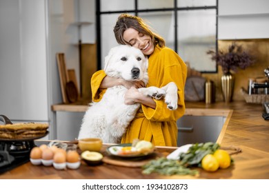 Young woman plays with her huge white dog while having a breakfast during a morning time on the kitchen at home - Powered by Shutterstock