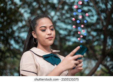 A young woman is pleased to get many positive reactions on her social media post. Standing outside at a park.