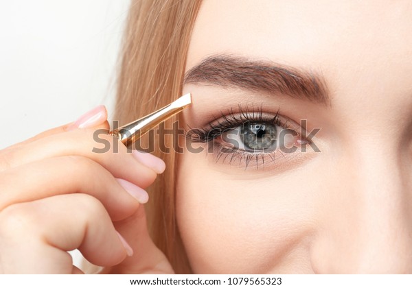 Young woman\
plucking eyebrow with tweezers,\
closeup