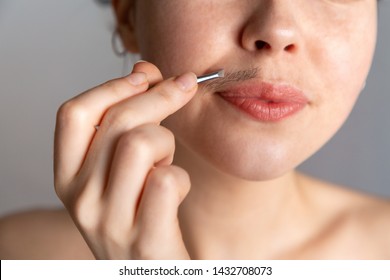 A young woman plucks her hair over her upper lip with tweezers. The concept of getting rid of unwanted facial hair