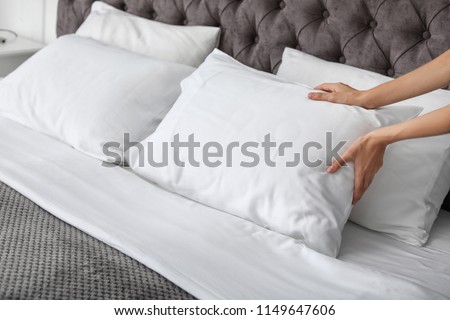 Young woman plumping white pillow on bed, closeup