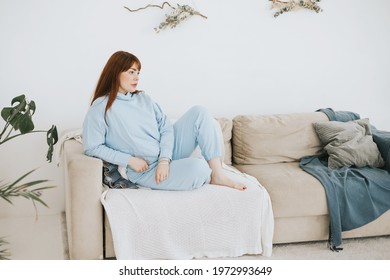 Young Woman Plus Size Model In A Blue Suit Having Rest On The Couch In A Modern Light Interior With Home Garden And Macrame On The Wall