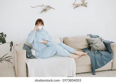 Young Woman Plus Size Model In A Blue Suit Drinking Coffee On The Couch In A Modern Light Interior With Home Garden And Macrame On The Wall