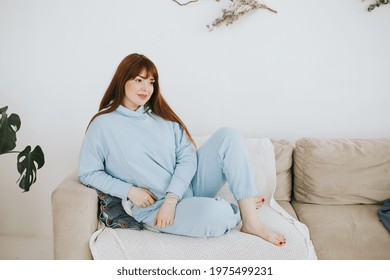 Young Woman Plus Size Model In A Blue Suit Having Rest On The Couch In A Modern Light Interior With Home Garden And Macrame On The Wall