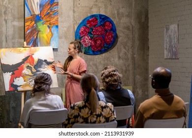 Young Woman Pointing At Painting And Presenting The Modern Art For People During Presentation In Art Gallery