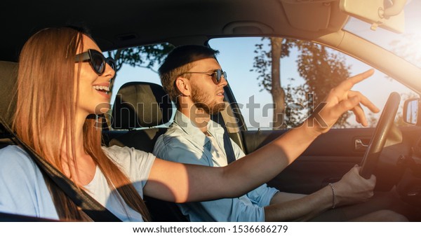 Young woman is pointing\
at something interesting she has noticed ahead while her boyfriend\
driving a car