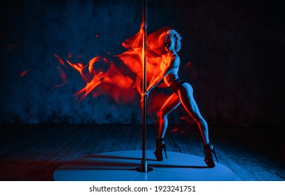 Young woman pole dancer in dark interior. Red fire motion effect. Tattoo on body.
