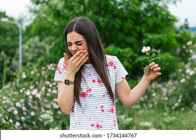 Young Woman With Pollen Allergy Holding A Flower And Saying No.. Young Woman With Pollen And Grass Allergies. Flowering Trees In Background. Spring Seasonal Allergies And Health Problems.