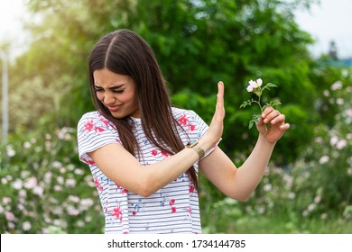 Young Woman With Pollen Allergy Holding A Flower And Saying No.. Young Woman With Pollen And Grass Allergies. Flowering Trees In Background. Spring Seasonal Allergies And Health Problems.