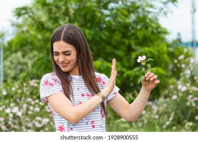 Young Woman With Pollen Allergy Holding A Flower And Saying No.. Young Woman With Pollen And Grass Allergies. Flowering Trees In Background. Spring Seasonal Allergies And Health Problems.