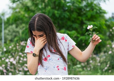 Young Woman With Pollen Allergy Holding A Flower And Saying No.. Young Woman With Pollen And Grass Allergies. Flowering Trees In Background. Spring Seasonal Allergies And Health Problems.