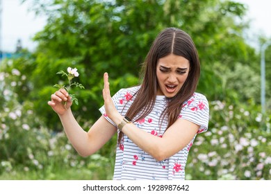 Young Woman With Pollen Allergy Holding A Flower And Saying No.. Young Woman With Pollen And Grass Allergies. Flowering Trees In Background. Spring Seasonal Allergies And Health Problems.