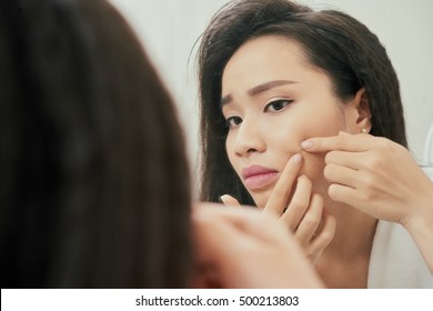 Young Woman Popping Pimple On Her Cheek