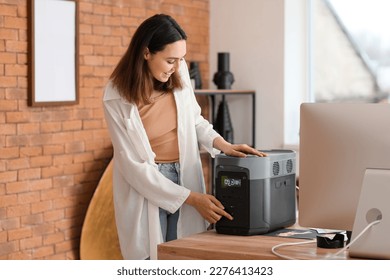 Young woman with portable power station at table in office - Shutterstock ID 2276413423