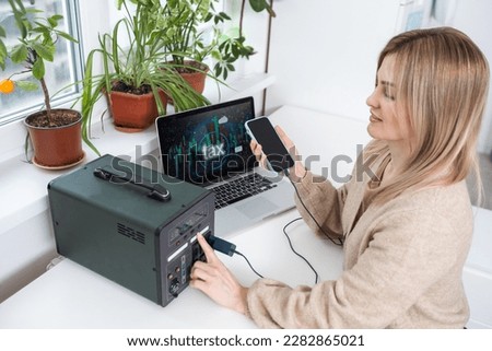 Young woman with portable power station at table in office.