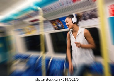 Young Woman Portrait Inside Underground In London Listening To Music With Earphones. Defocused Image With Radial Blur.