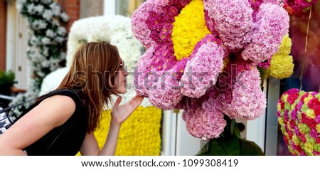 A young woman poses in front of a flower display at a local Chelsea shop in London, UK as part of a popular flower show every May